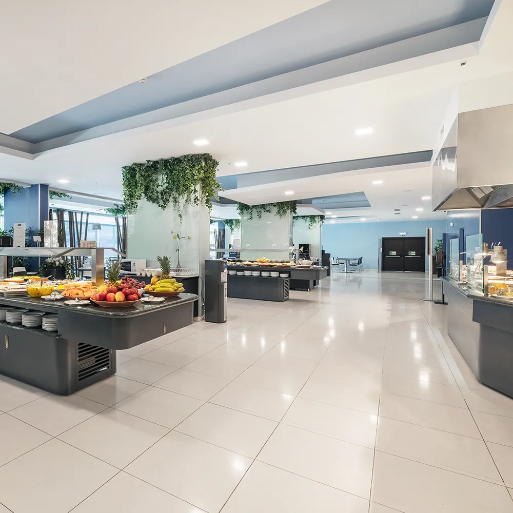 Spacious hotel restaurant dining area with a central buffet, tables and large windows overlooking the outdoor area