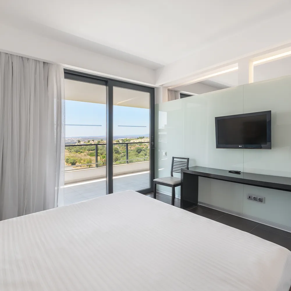 Vista desde la cama de la Suite Classic del Alvor Baía con televisor de pared y balcón con vistas al interior.