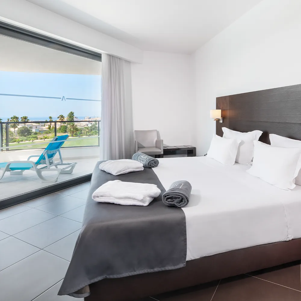 Quarto principal da Suite Club do Alvor Baía com cama de casal e acesso à varanda.