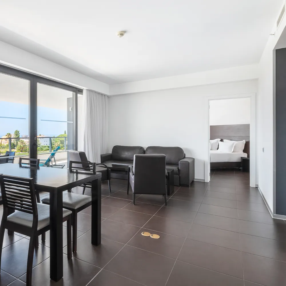 Sala de estar da Suite Club do Alvor Baía com sofá, zona de refeições e varanda com vista para a piscina.