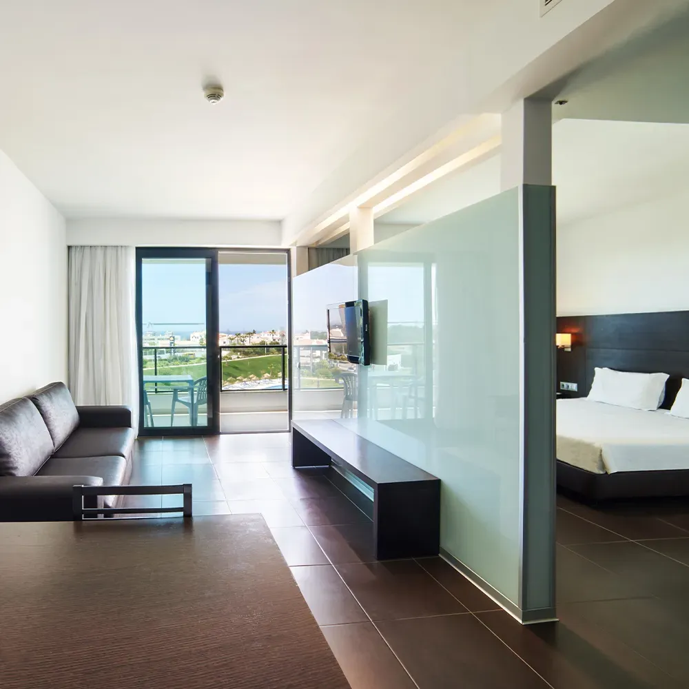 Sala de estar da Suite Prestige do Alvor Baía com sofá-cama, TV e mesa de refeições.