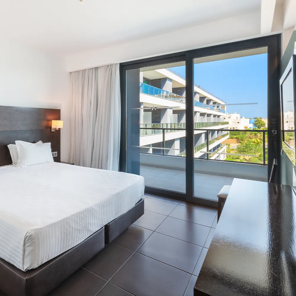 Quarto da Suite Prestige do Alvor Baía com cama de casal e varanda com vista lateral para a piscina e jardim.