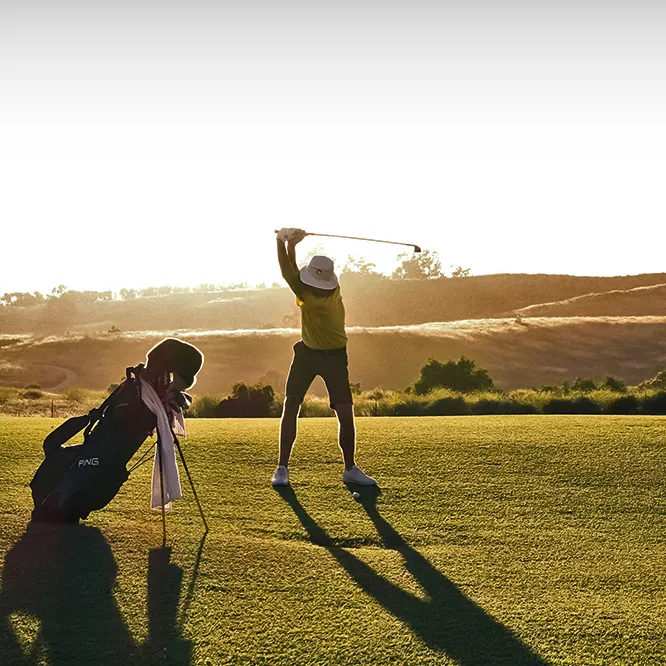 Personne jouant au golf sur un parcours au coucher du soleil.