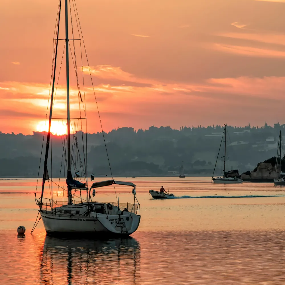 Alvor Ria at sunset, with sailing boats and anchored vessels.