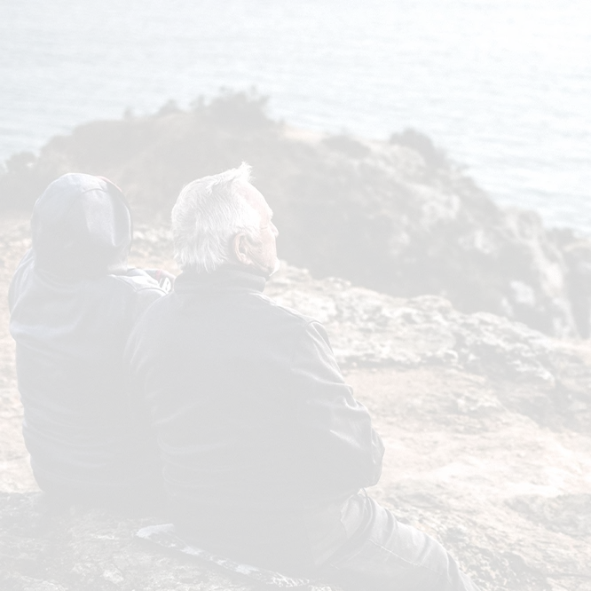 Casal sénior sentado numa falésia, contemplando o pôr do sol com o oceano à sua frente