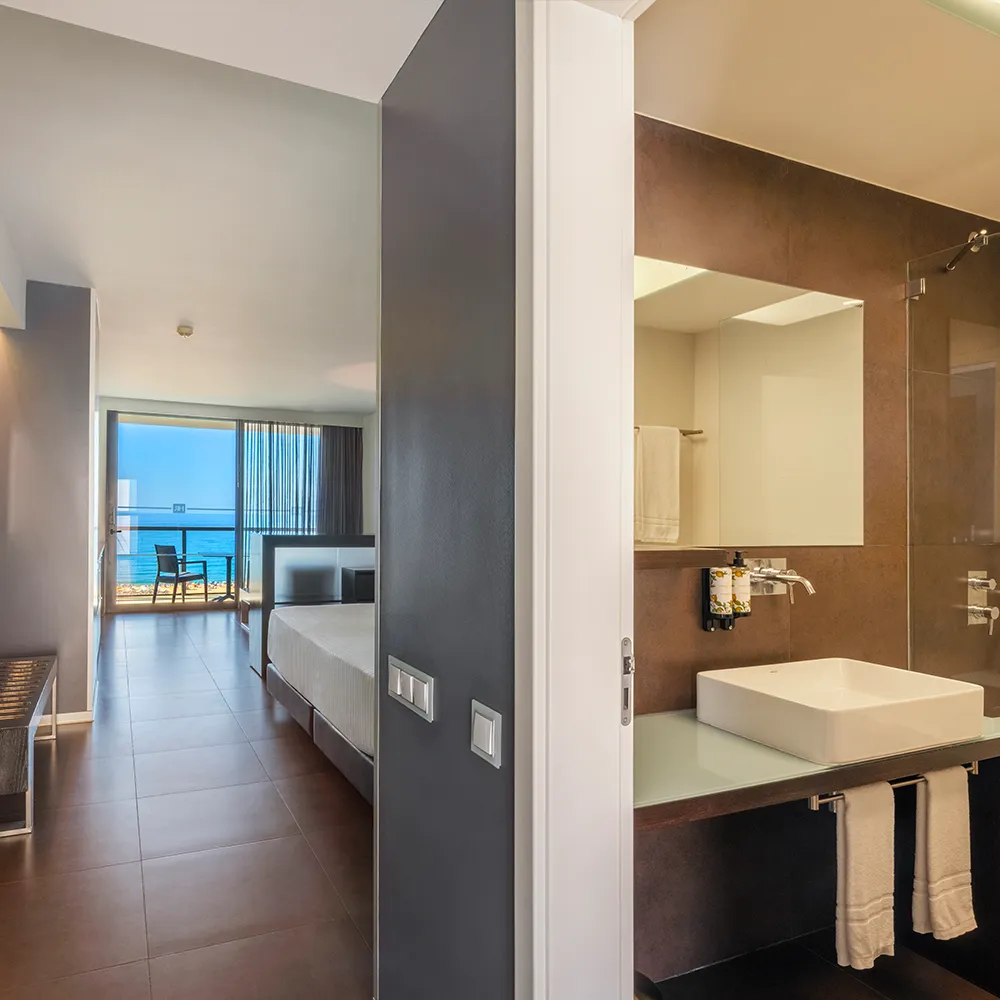Entrance to the Suite Deluxe at RR Hotel da Rocha with the bathroom in the foreground and a balcony overlooking the sea.