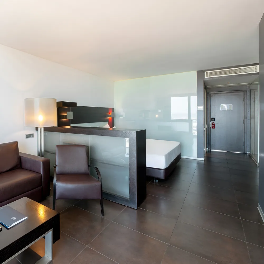 Zona de estar de la Suite Prestige con sofá, sillón de cuero y separador de cristal.